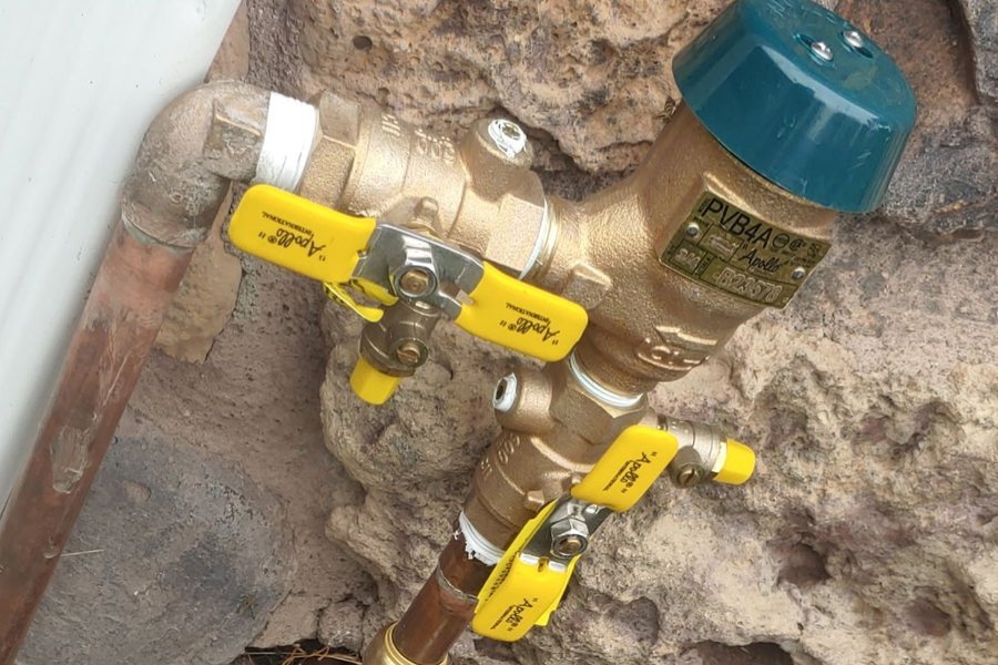 Apollo pressure vacuum breaker backflow preventer on copper pipe against a stone wall